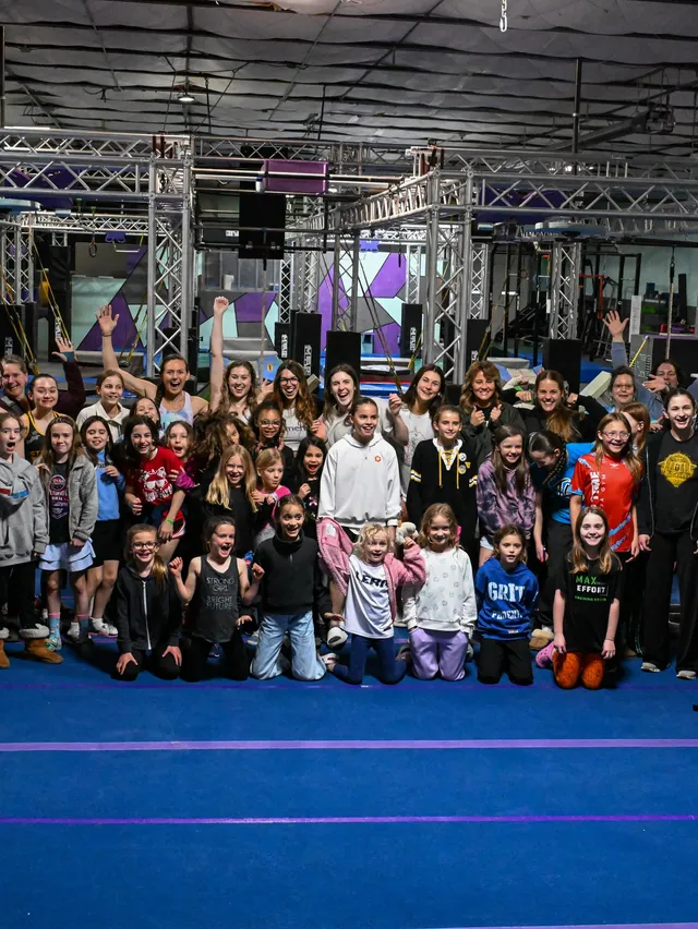 A big group of girls and women cheering and waving together on the mats