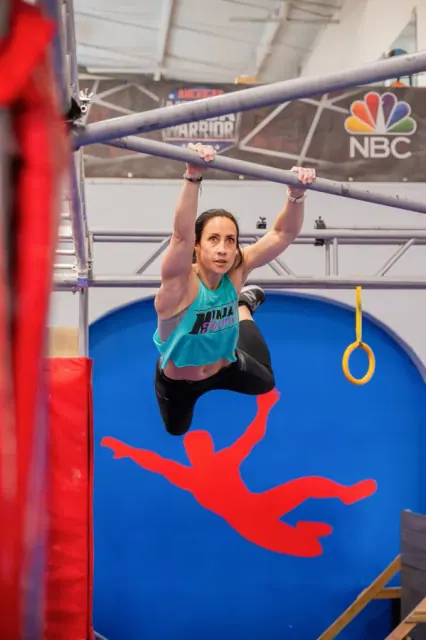 An athlete hanging from a bar above a blue and red mat