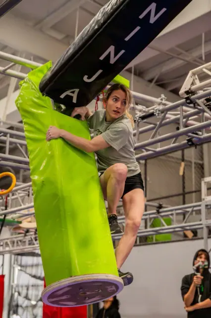 An athlete wrapped around a lime-green padded pole obstacle