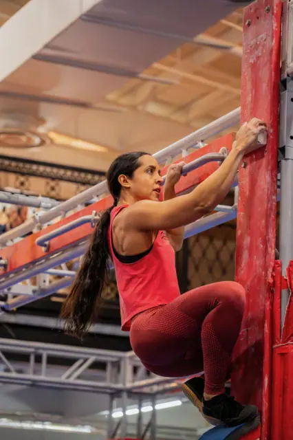 An athlete climbing a red wall obstacle