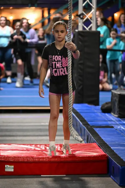 A young athlete in a For the Girls shirt standing on a pillar obstacle