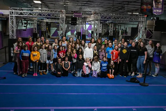A large group of girls and women athletes posing together on the mats in a ninja gym