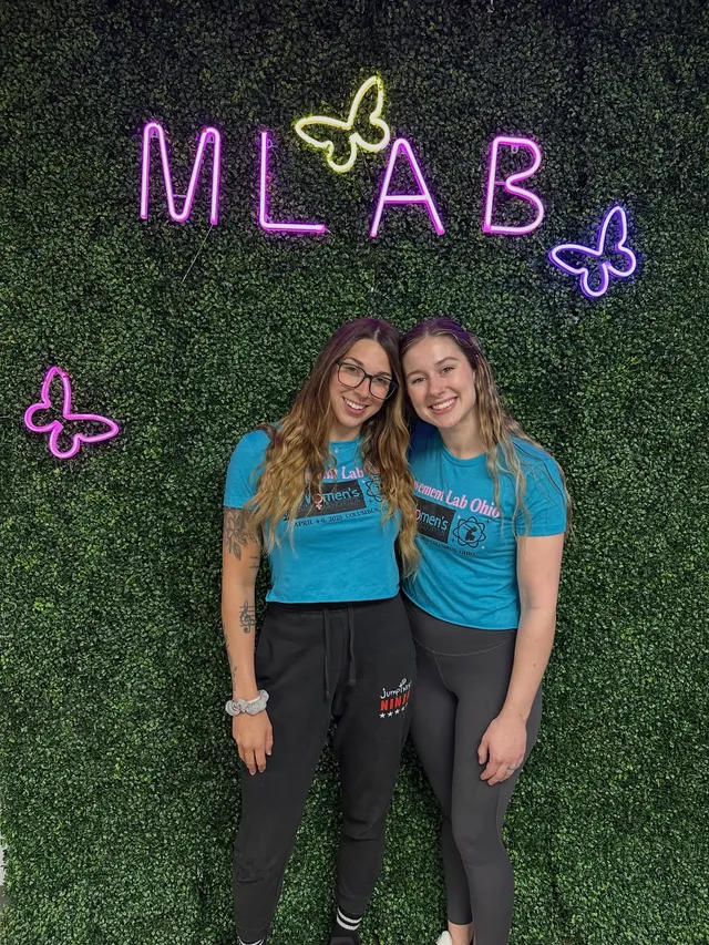 Megan Budway and Jennifer Sanders in matching blue WNA event shirts under the neon MLAB sign