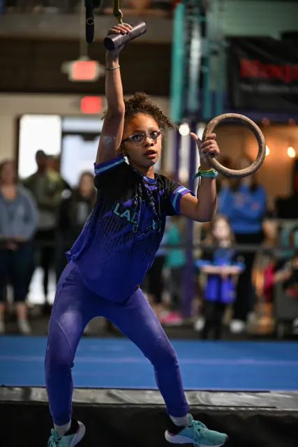 An athlete in blue reaching for a hanging ring