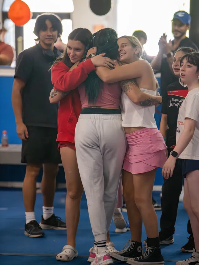 Three athletes sharing a group hug as friends and family look on