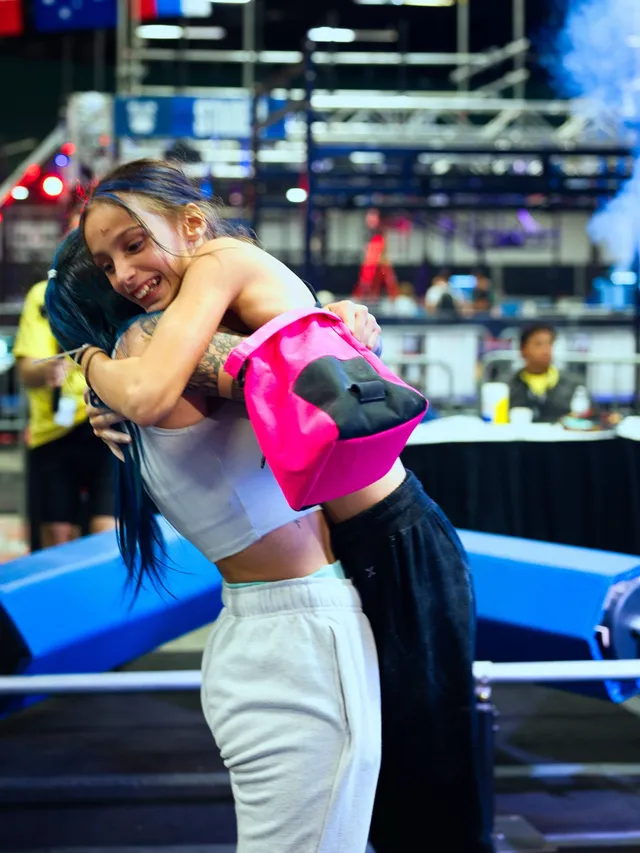 A young athlete with a pink chalk bag hugging a coach after her run