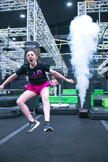 An athlete jumping off a platform as a smoke cannon fires behind her