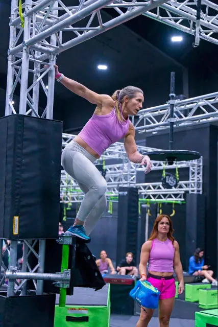 An athlete leaping between platforms on a truss-framed course