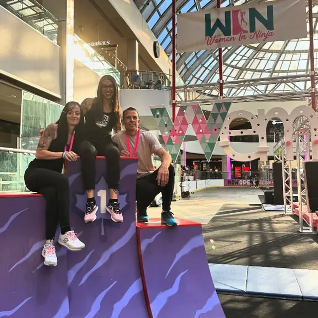 Megan and two members of the Women in Ninja team sitting on a purple obstacle at West Edmonton Mall